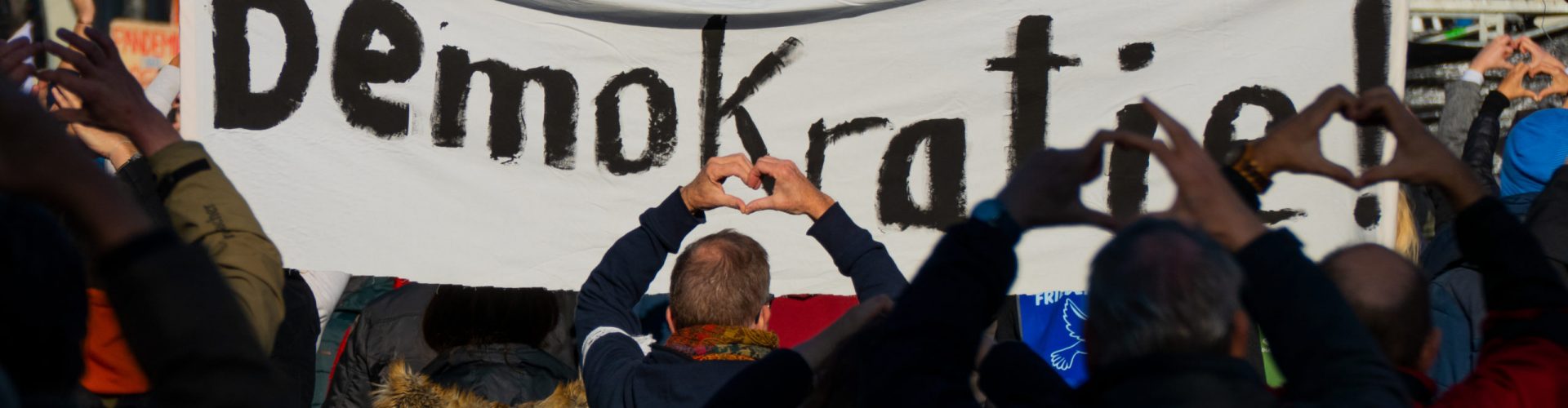 Leipzig, Germany - November 07, 2020: At a demonstration against the German government's measures against the coronavirus, the hands of the demonstrators form hearts, in the background you can see a sign with " Democracy " written on it